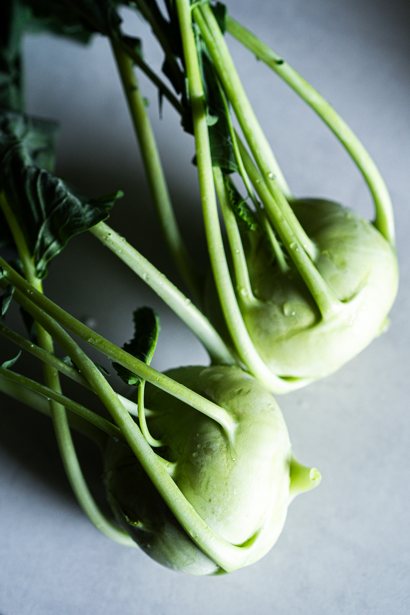Zwei frische Kohlrabi mit langen grünen Stielen und Blättern, mit Wassertropfen auf hellgrauem Untergrund