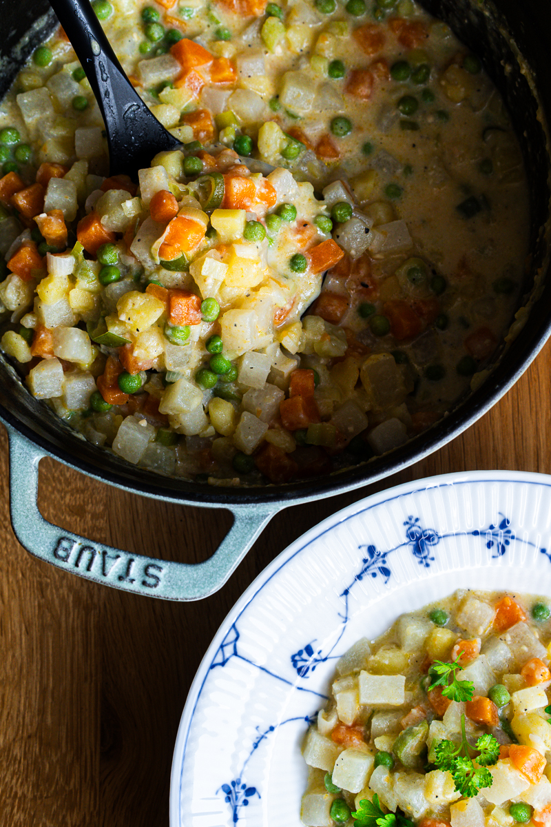 Gemüseeintopf mit Miso im Topf mit schwarzer Kelle, daneben ein Teller mit Kartoffel-Kohlrabi-Eintopf und Petersilie
