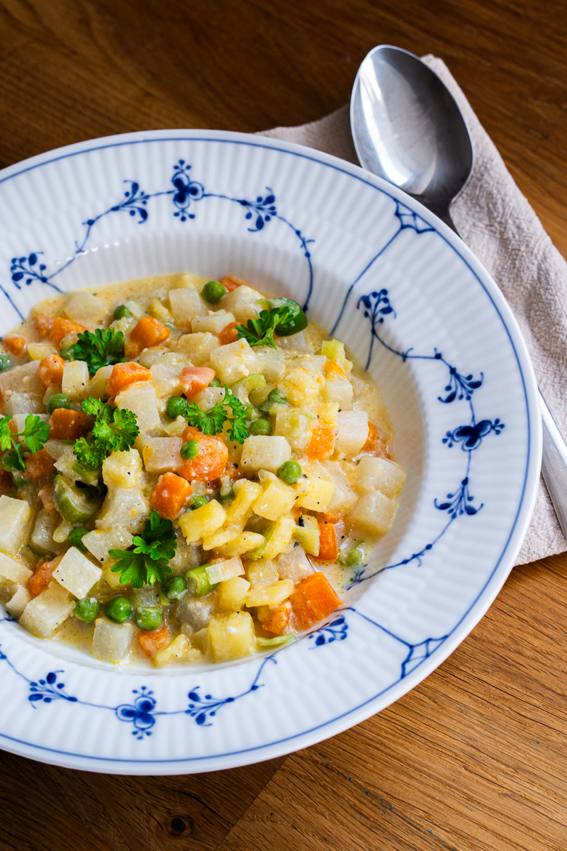 Miso-Gemüseeintopf mit Kohlrabi und Kartoffeln im blau-weißen Teller, mit Petersilie garniert, daneben ein Löffel